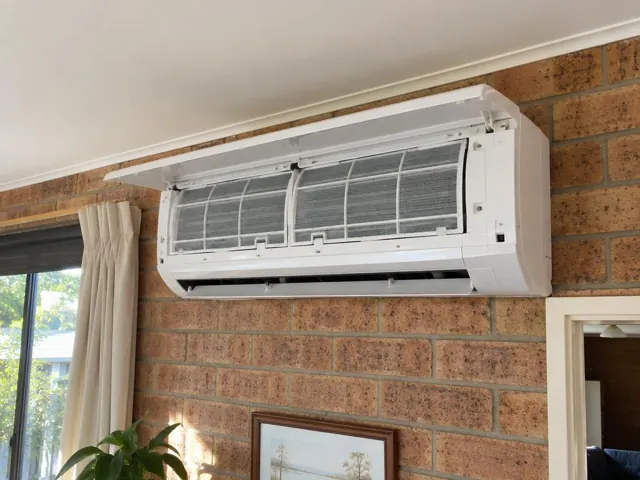 Clean split system indoor unit with open front panel and visible filters on a brick wall in Salisbury East